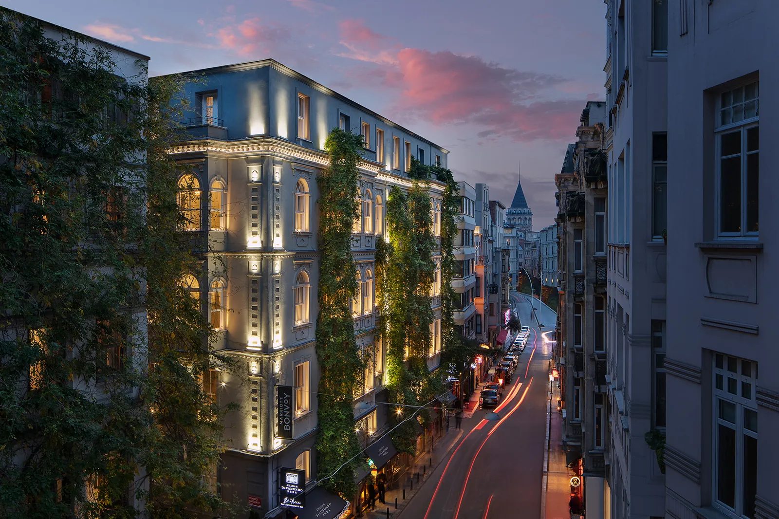 A restored Beyoğlu building with the Galata Tower behind it at dusk